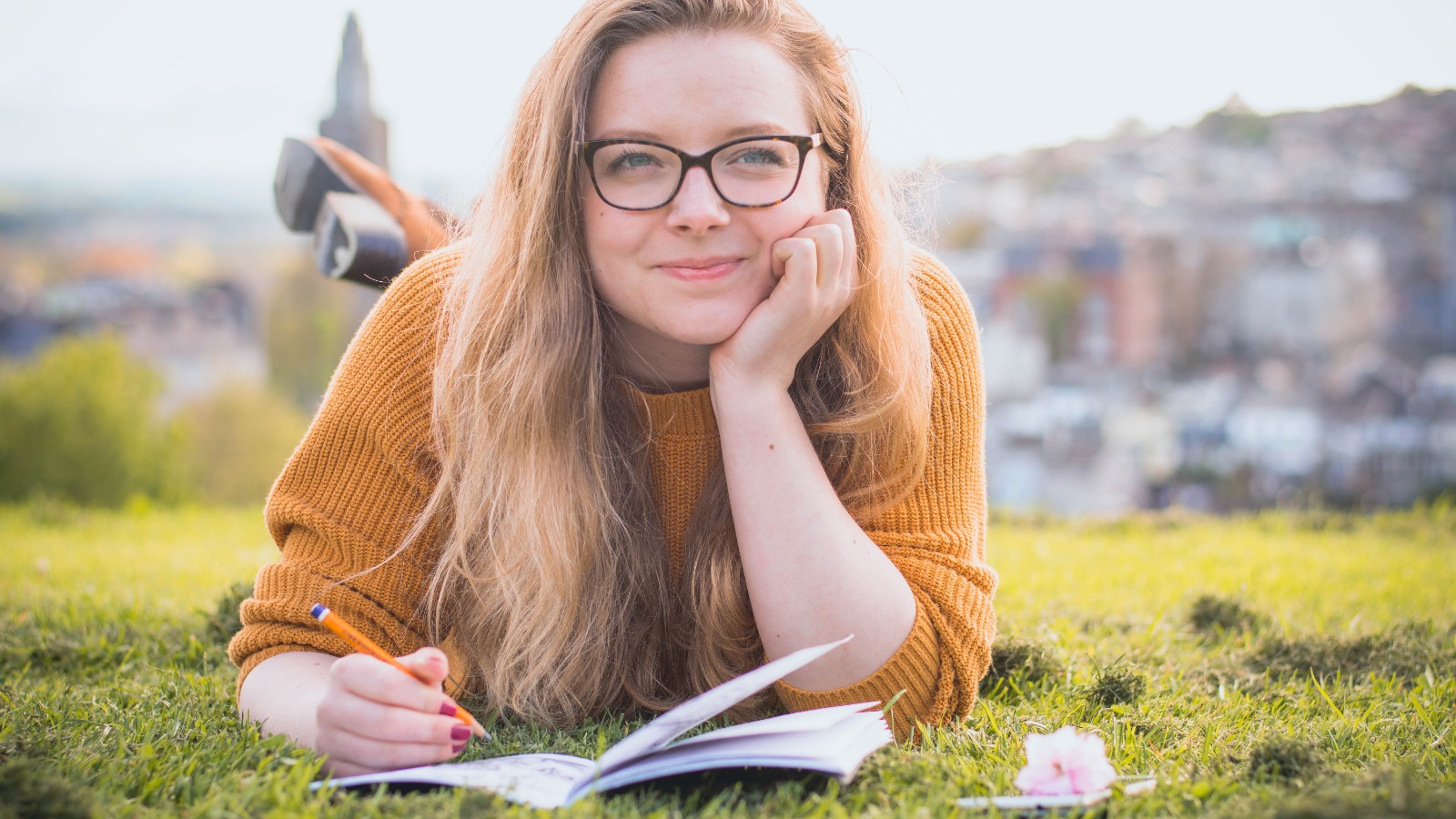 Foto “Woman Lying on Green Grass While Holding Pencil” von Liam Anderson