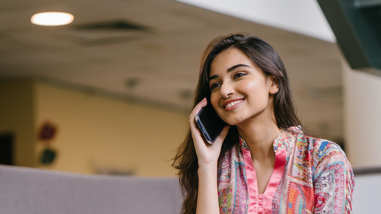 Foto “Photo of Smiling Woman in Floral Salwar Kameez Talking on Phone While Sitting on Edge of Wooden Table” von mentatdgt